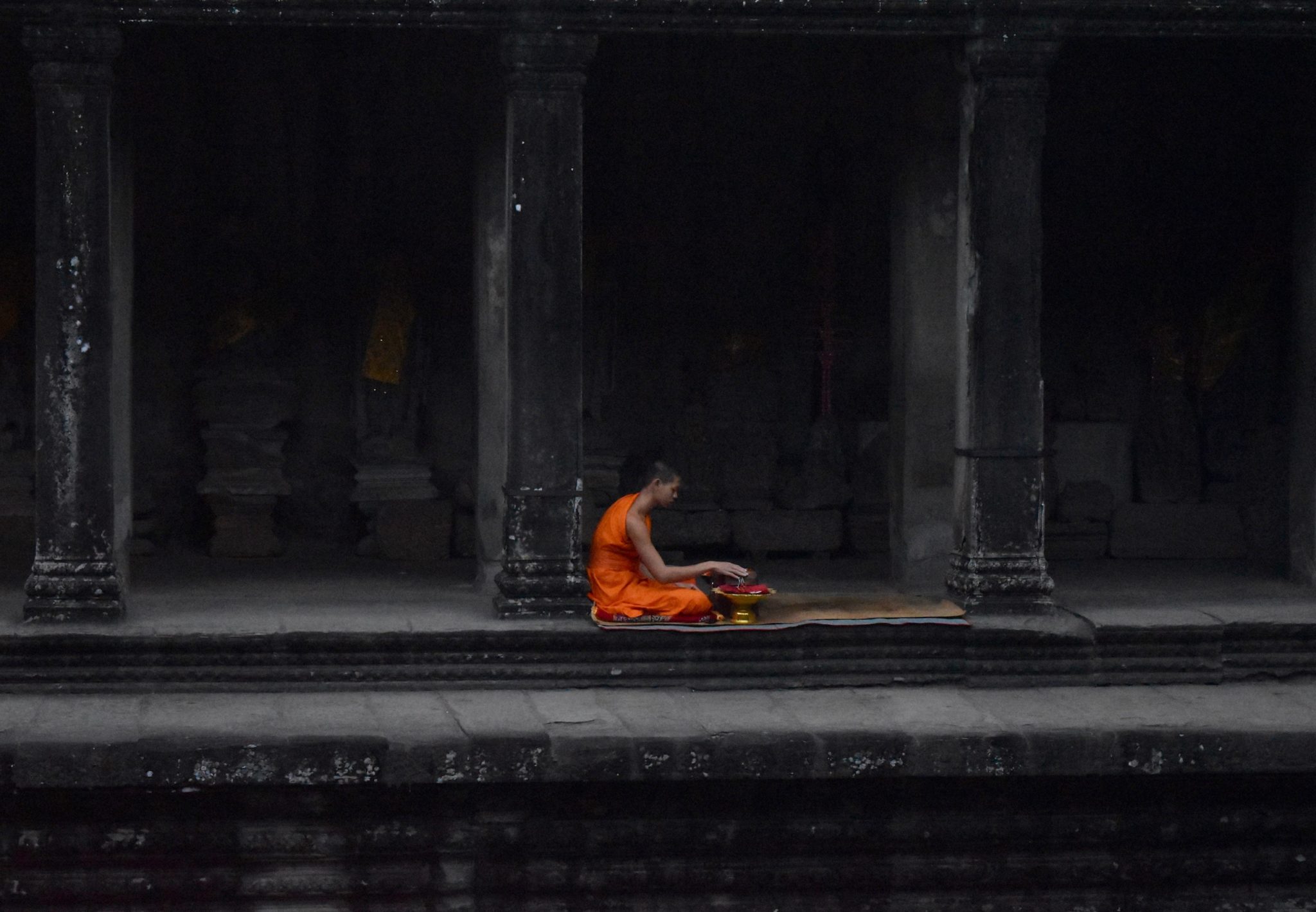A monk sitting in orange robes at Angkor Wat