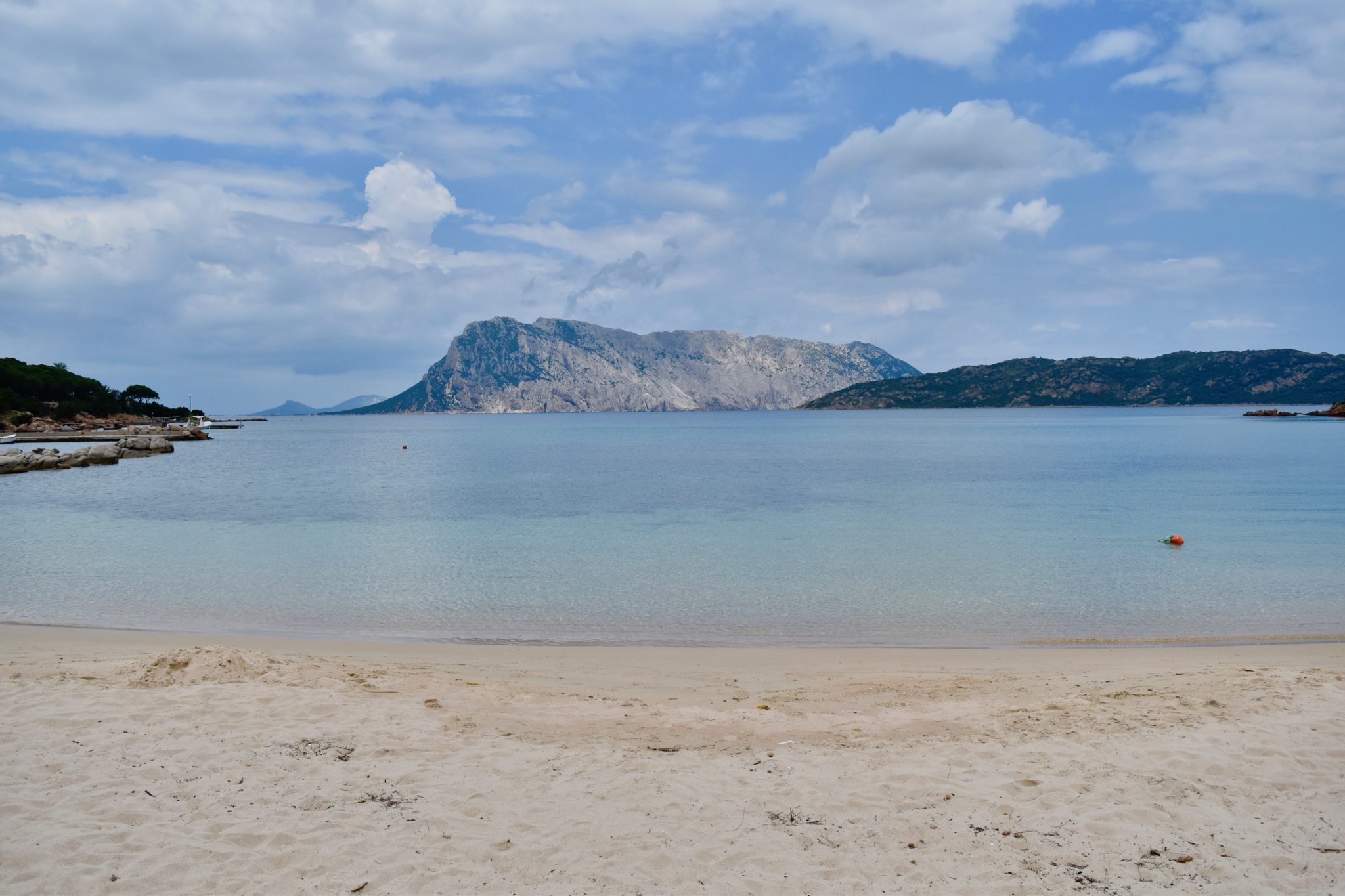 a sandy Sardinia beach with a rocky island in the distance