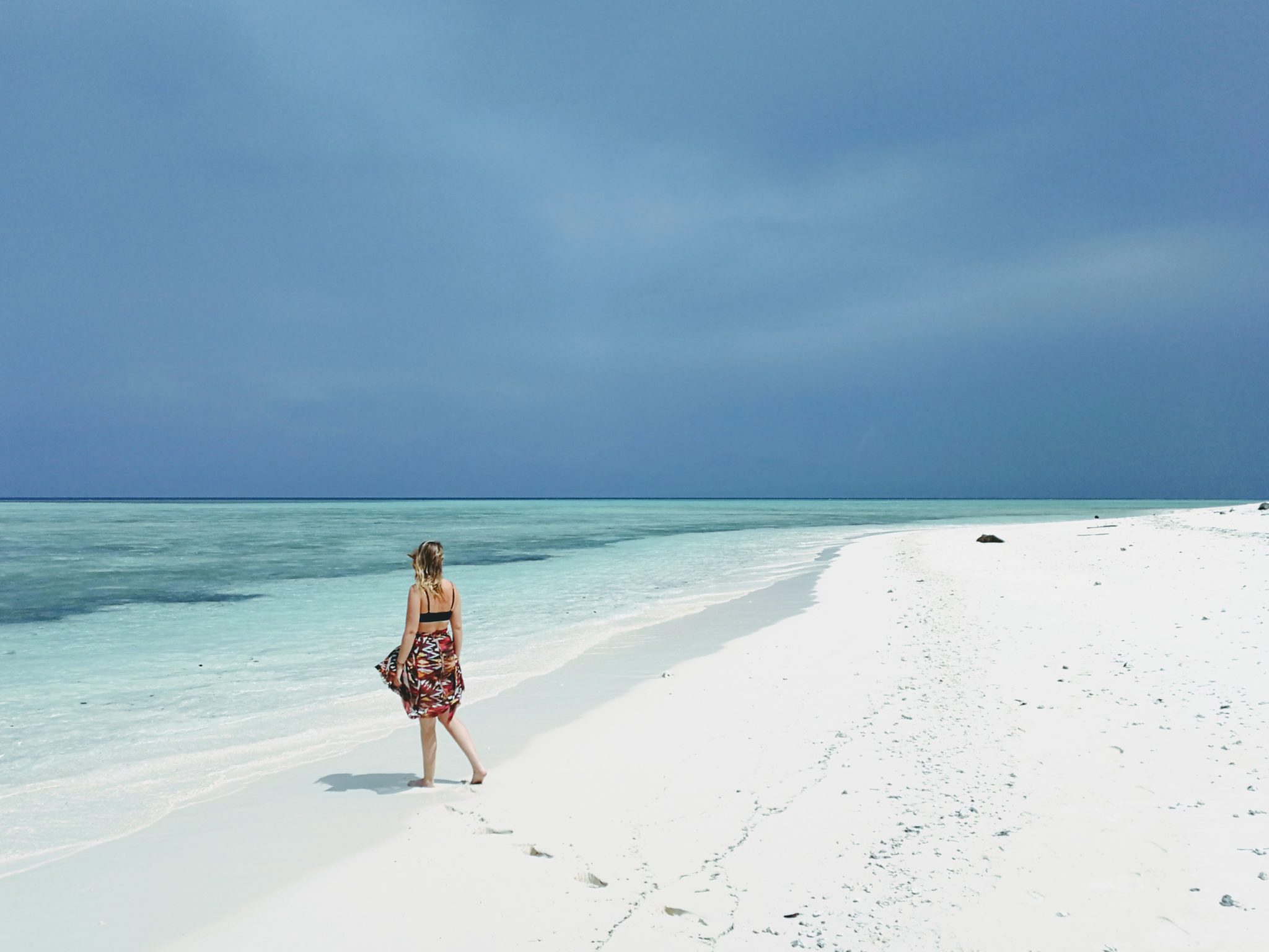 Sarah walking across a white sand beach towards crystal clear blue water