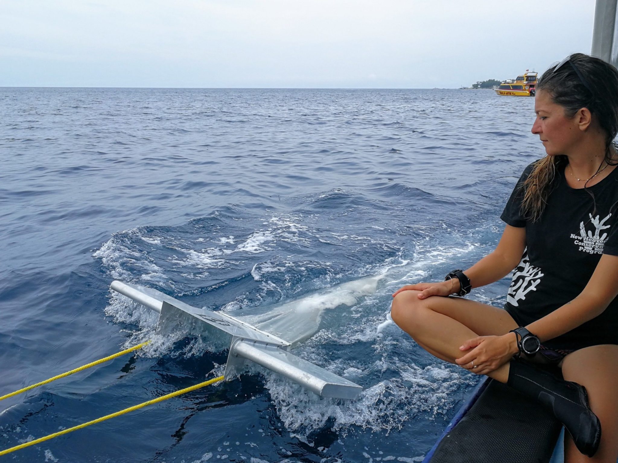 A woman sitting on the side of a boat, watching a trawling device