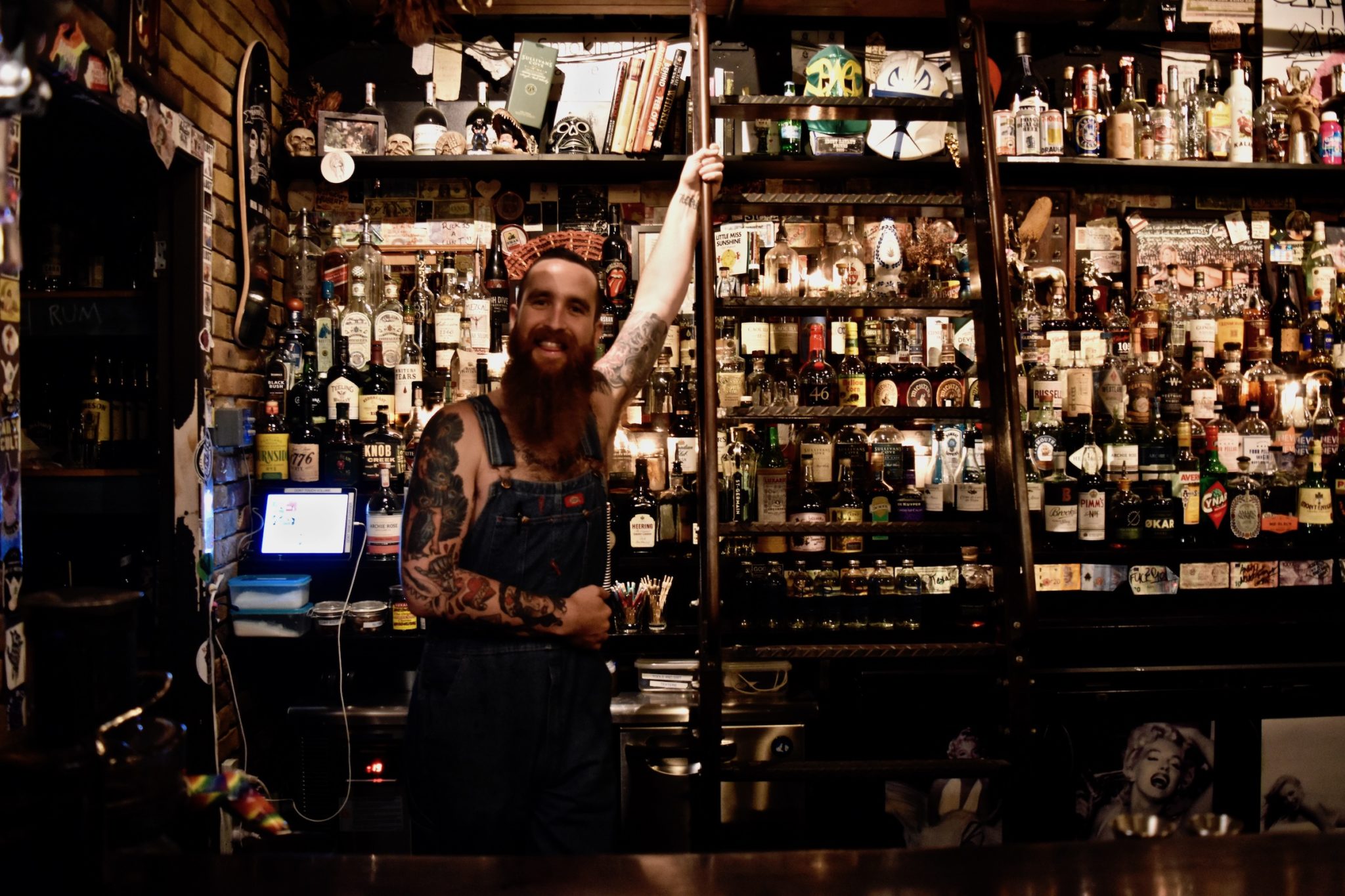 A bearded barman wearing dungarees 