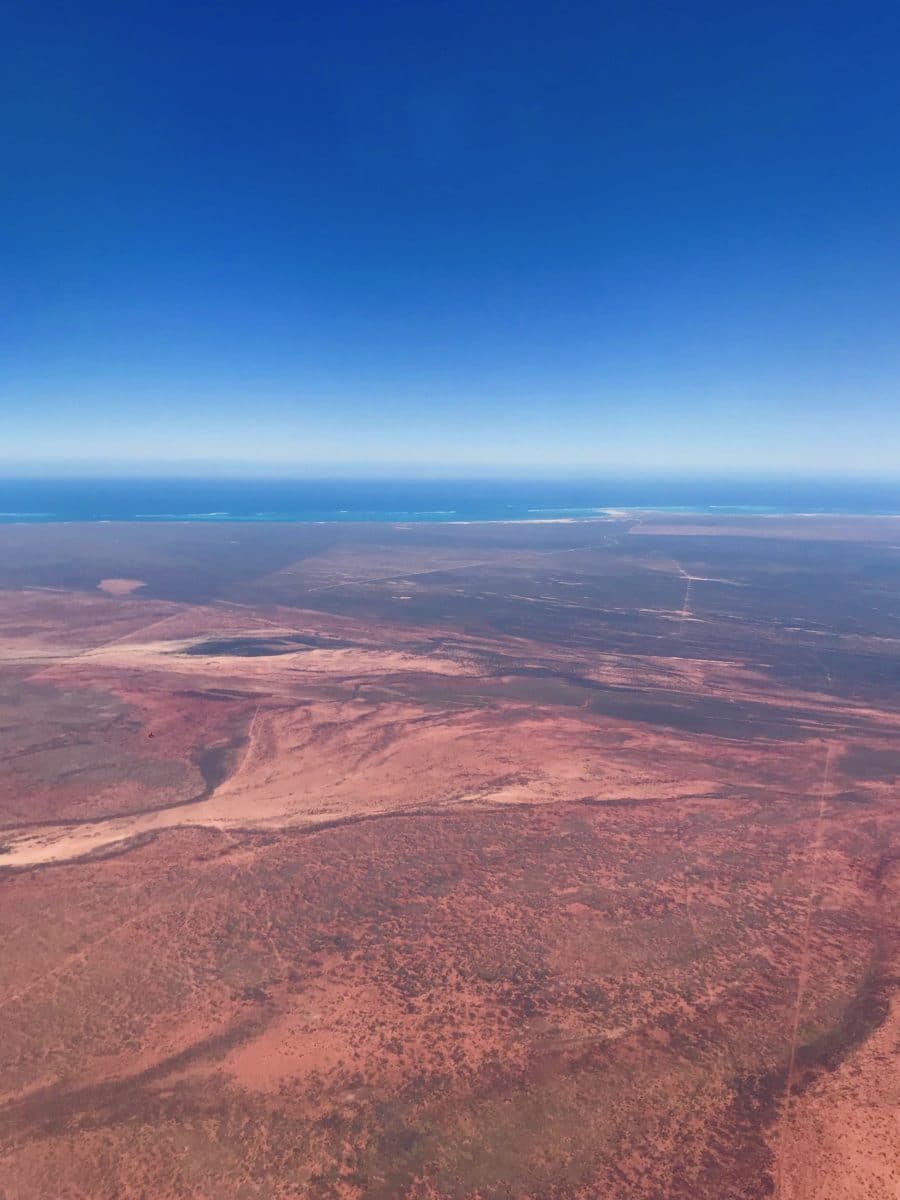 The view from a plane over red earth and blue ocean