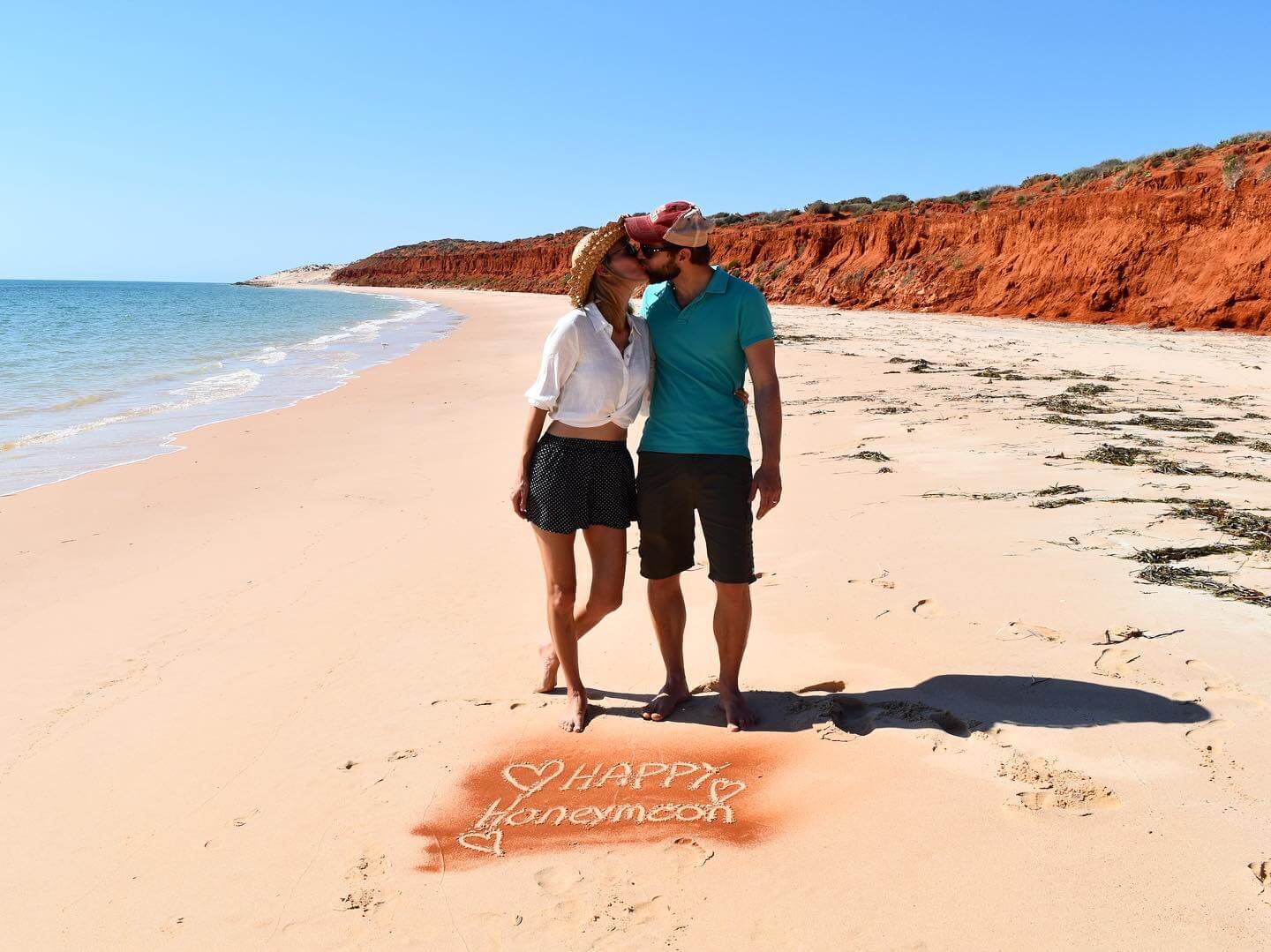 Hayley and Enrico on a beach in Western Australia with 'Happy Honeymoon' engraved in the sand