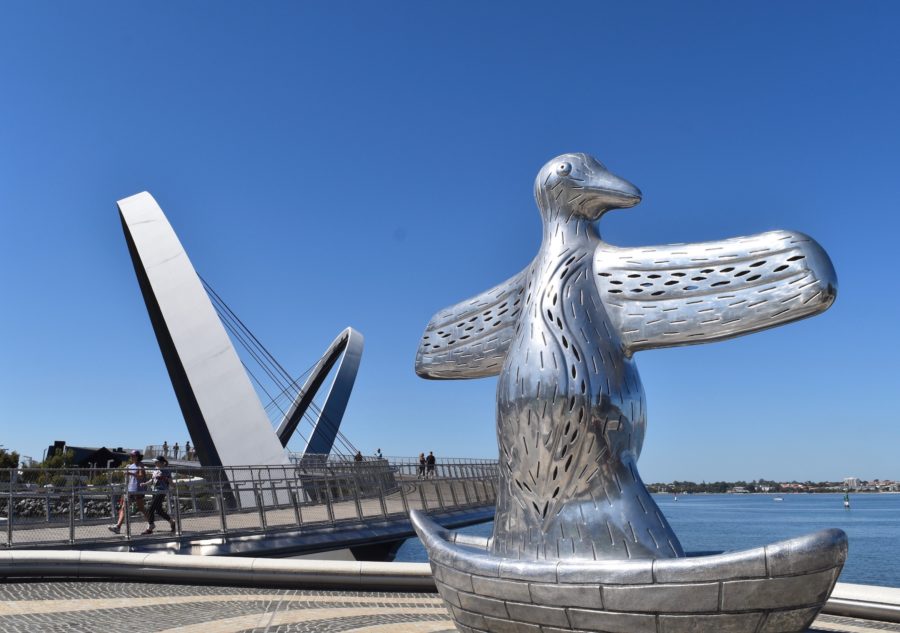 An iron sculpture of a bird on a boat by the water