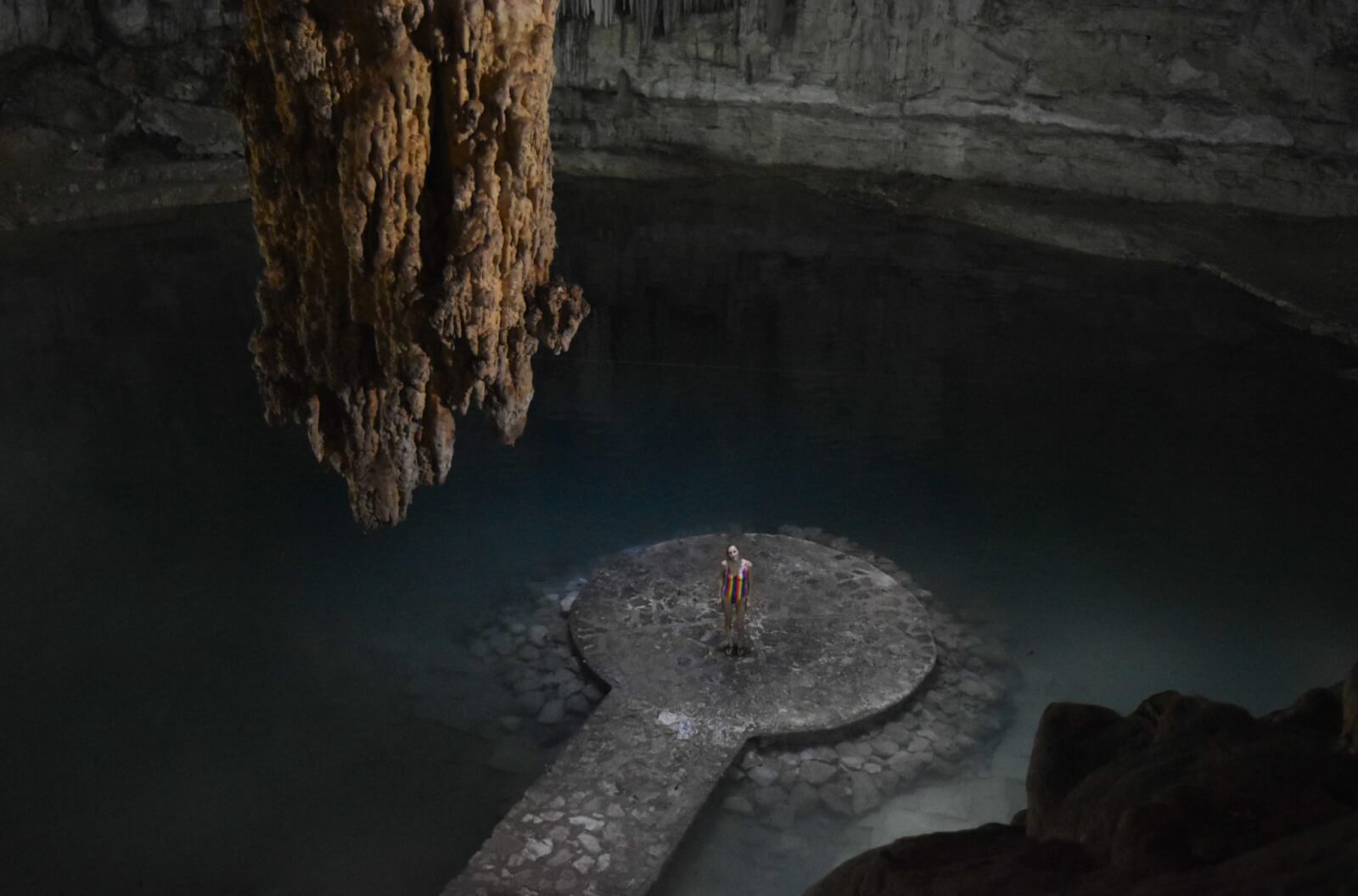 Hayley standing on a platform in a cave like cenote 