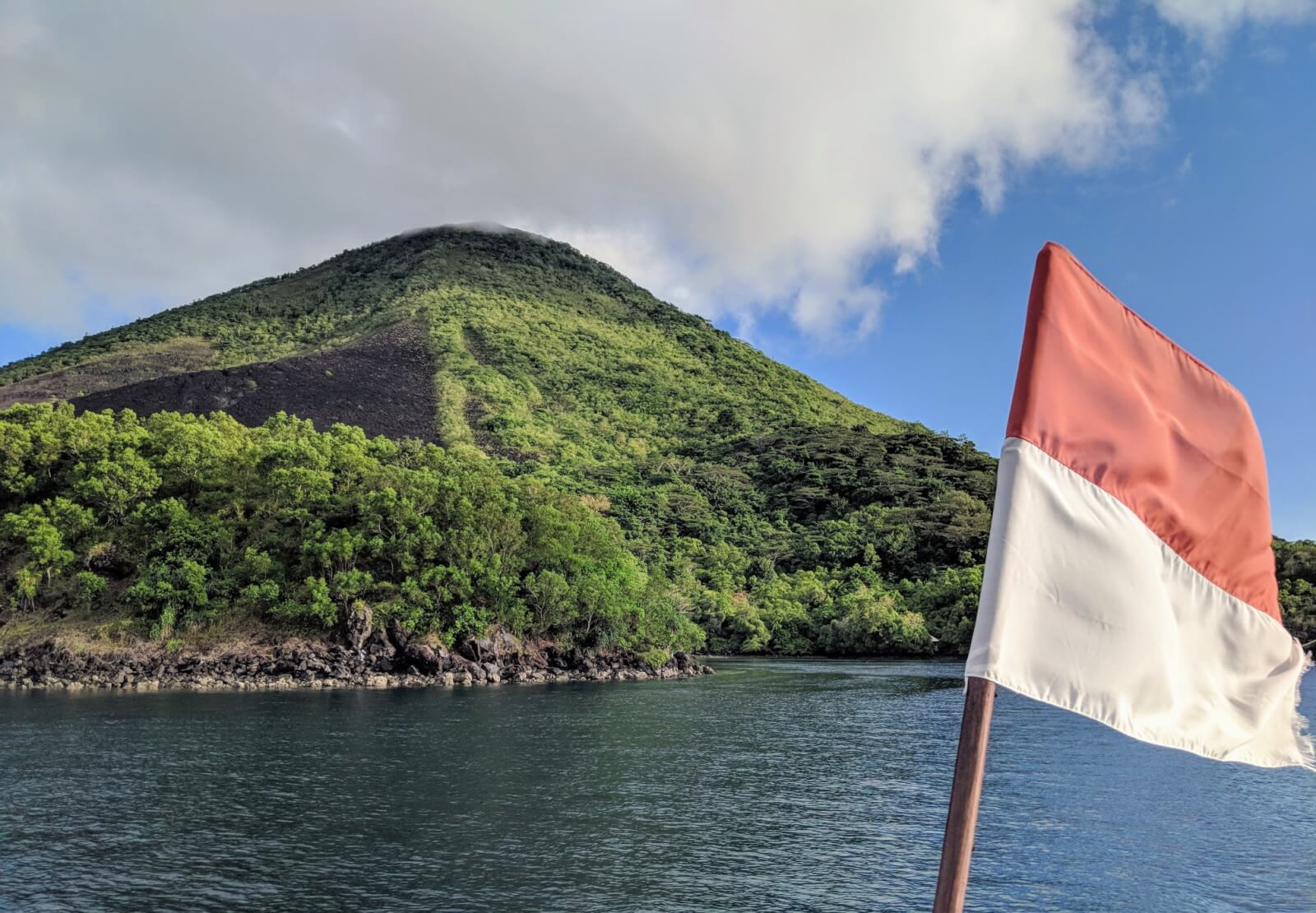 The Indonesian flag waving in front of a volcanic island 