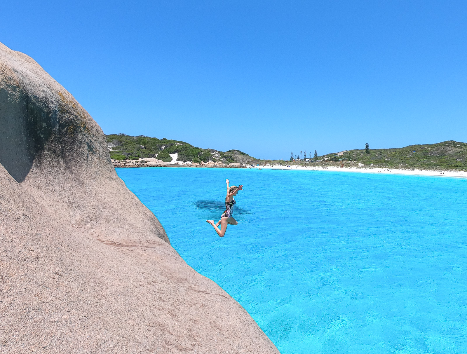 Hayley jumping off a rock into bright blue water at Twilight Beach 