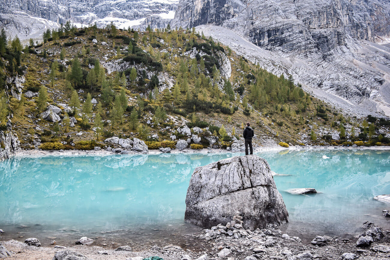 Enrico standing on a rock by a bright blue lake with a mountain backdrop