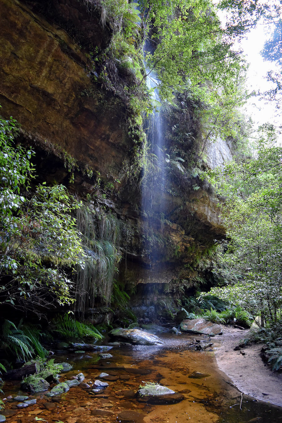 A narrow waterfall descending onto a path