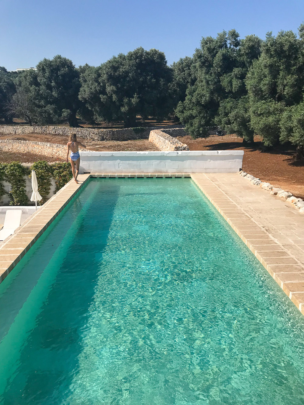 Hayley walking along the side of a beautiful pool surrounded by olive trees