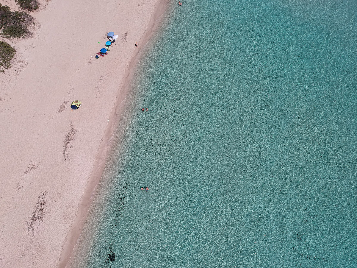 A beach with white sand and crystal clear water from above