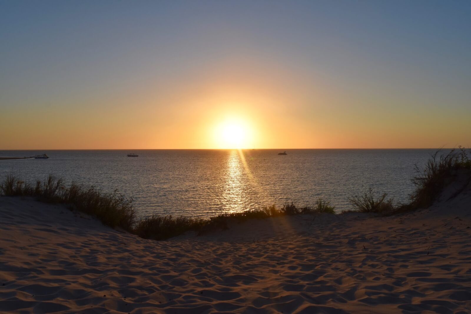 the sun setting into the ocean from a sandy beach