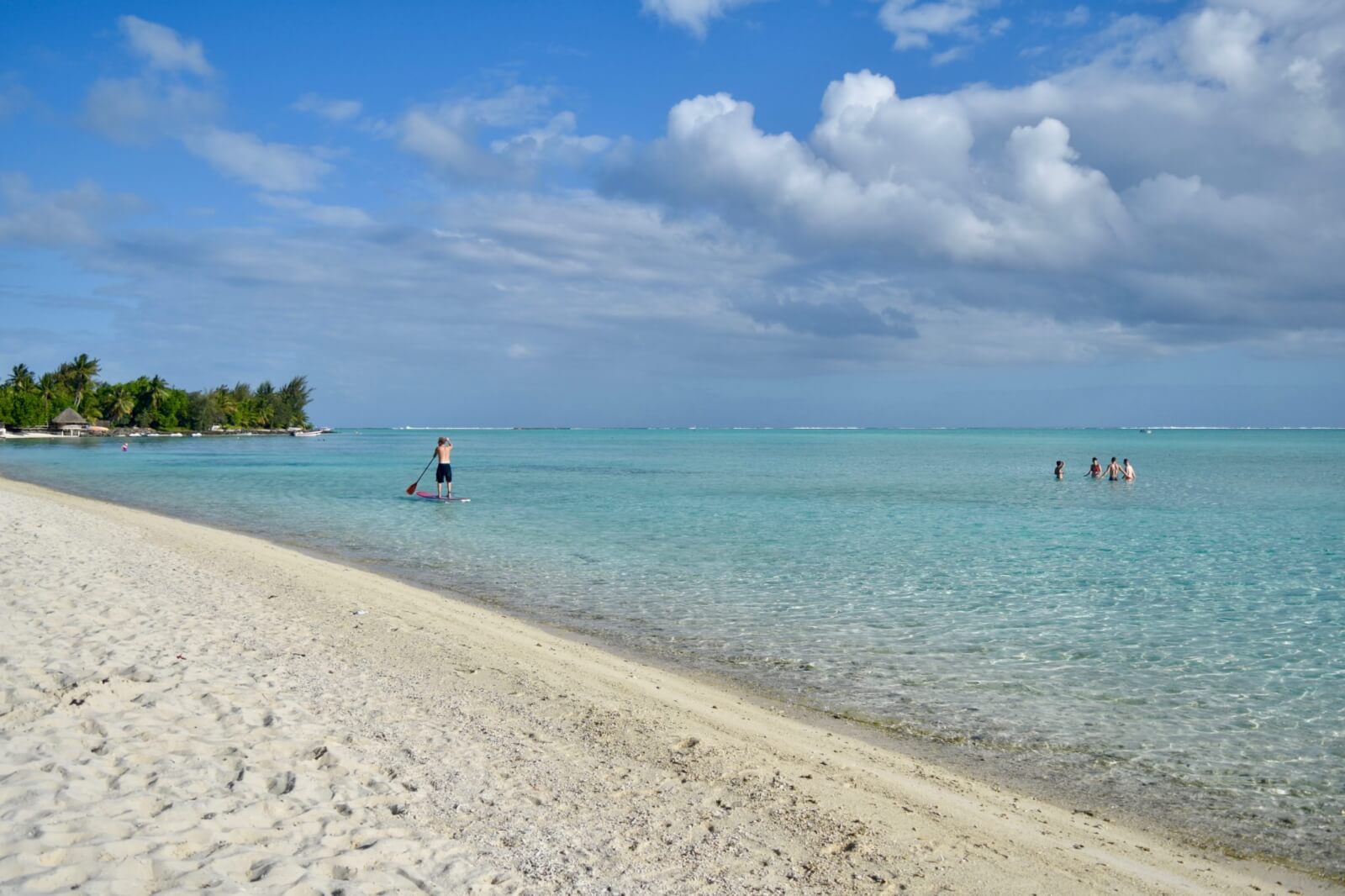 A white sand beach with clear water and a man on a SUP