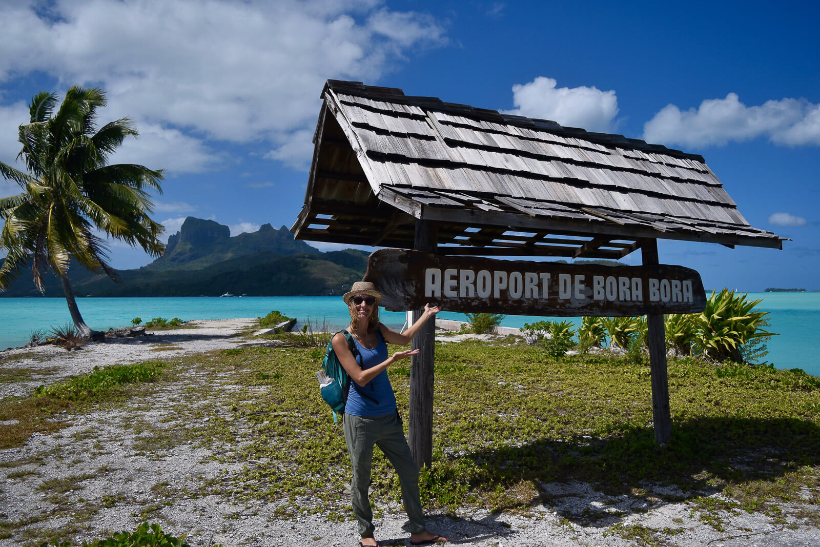Hayley standing next the the Bora Bora airport sign with the turquoise water in the background