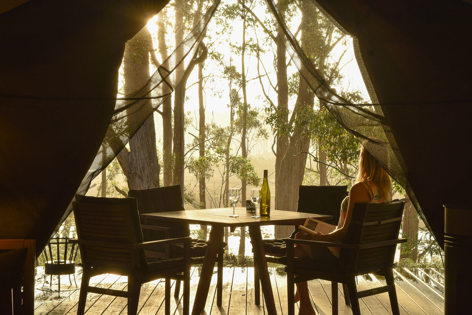 Looking out from a glamping tent onto a deck with a table and chairs and forest in the distance