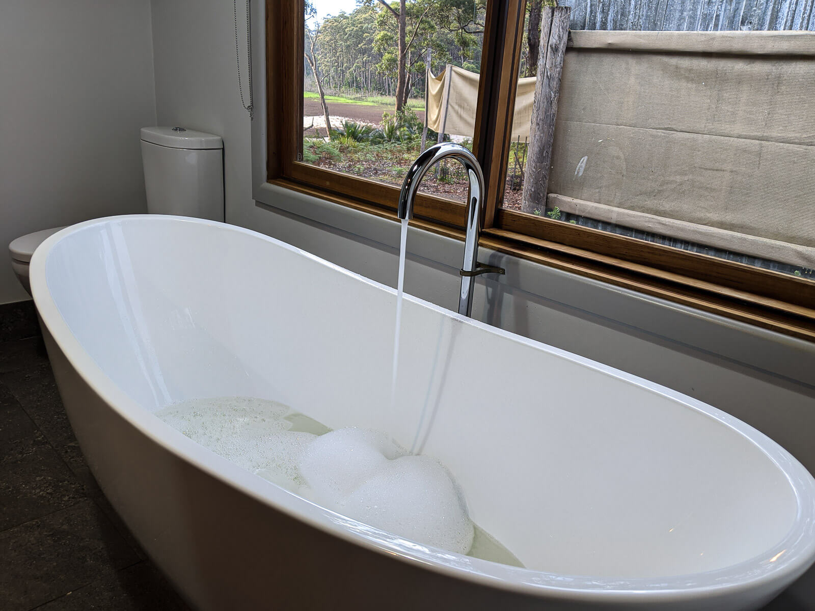 A large bath with a running tap and views outside of the window