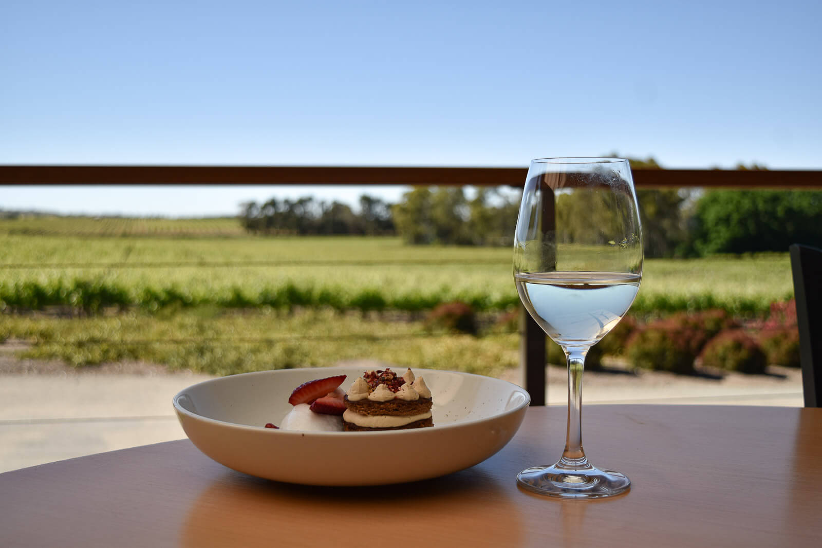 A glass of wine and dessert on a table overlooking Clare Valley vineyards