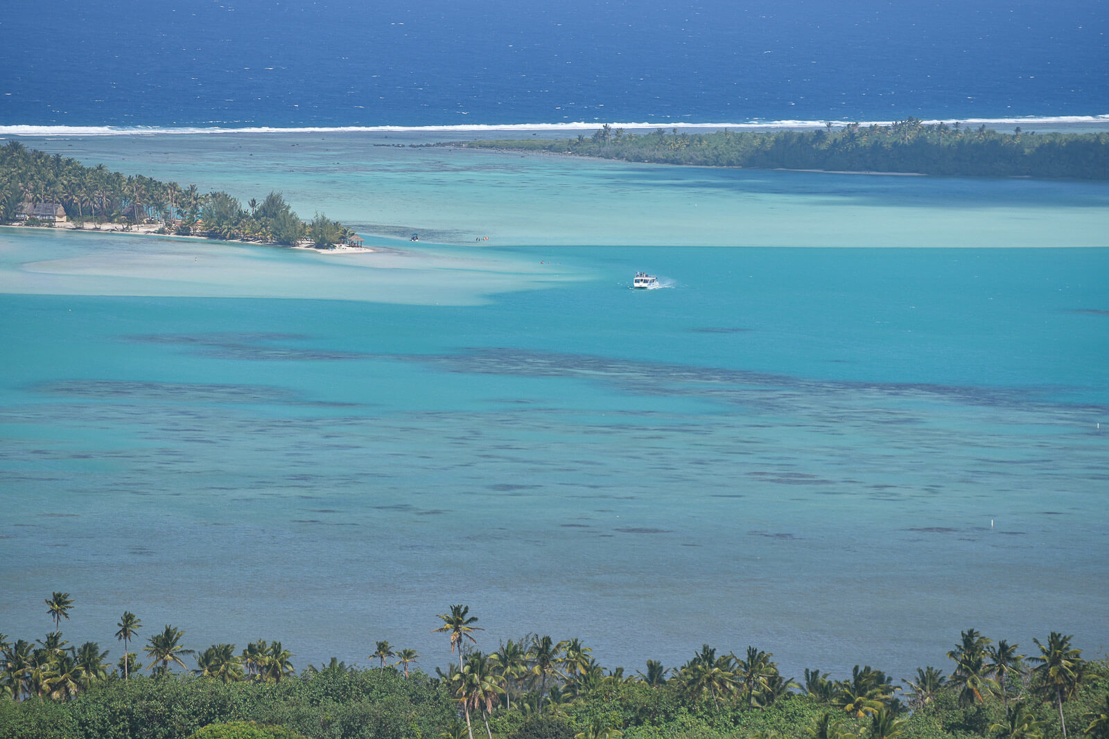 The Aitutaki Lagoon with many different shades of blue and a boat in the middle