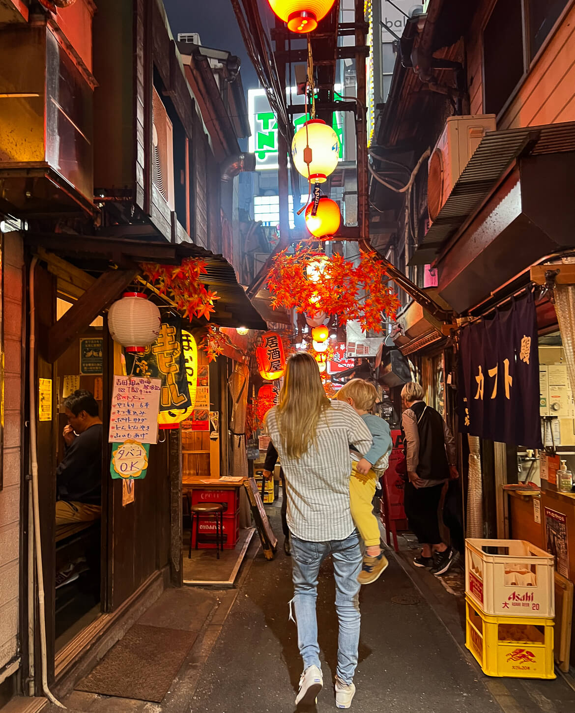 A woman walking through a Tokyo laneway with a toddler