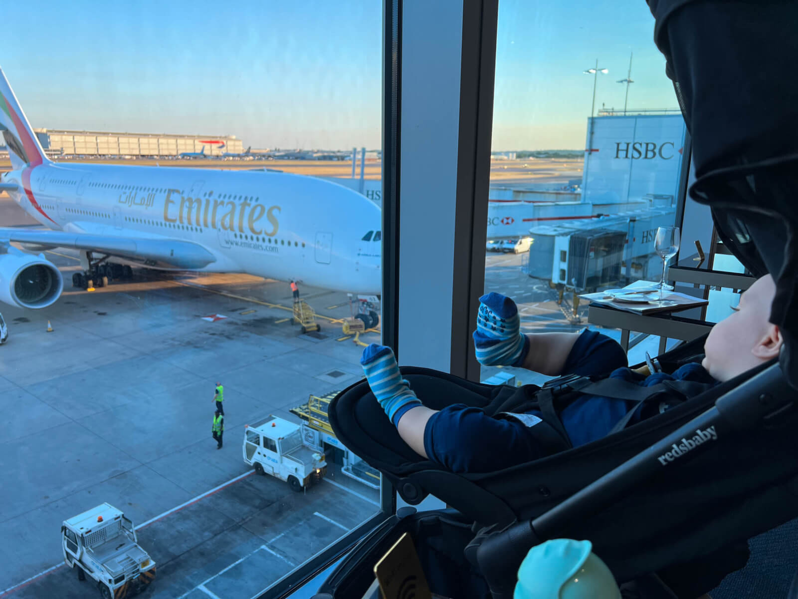 A baby in a pram looking out at an aeroplane before a long haul flight