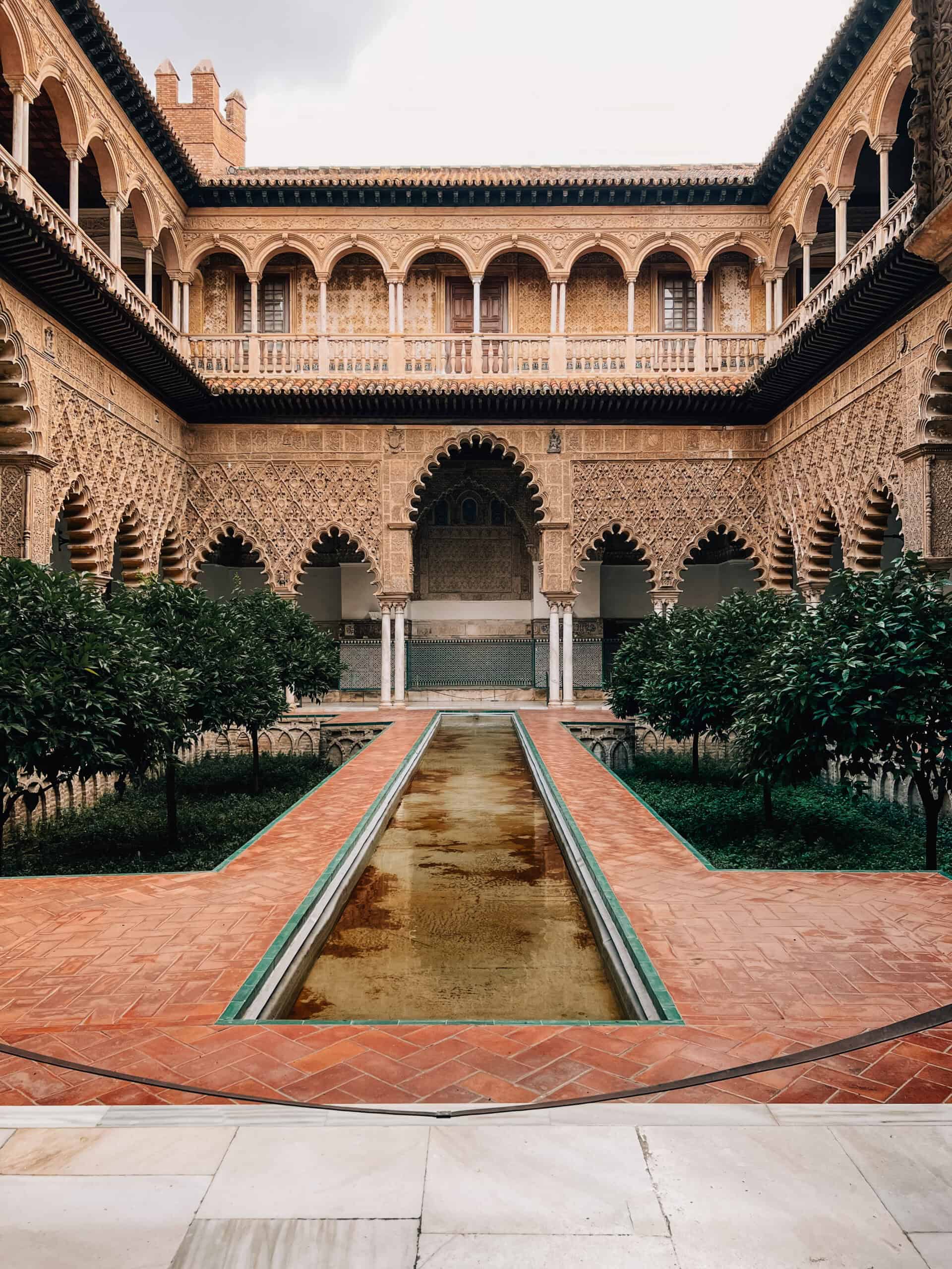 Central Alcázar courtyard with long water channel, orange trees and carved arcades.