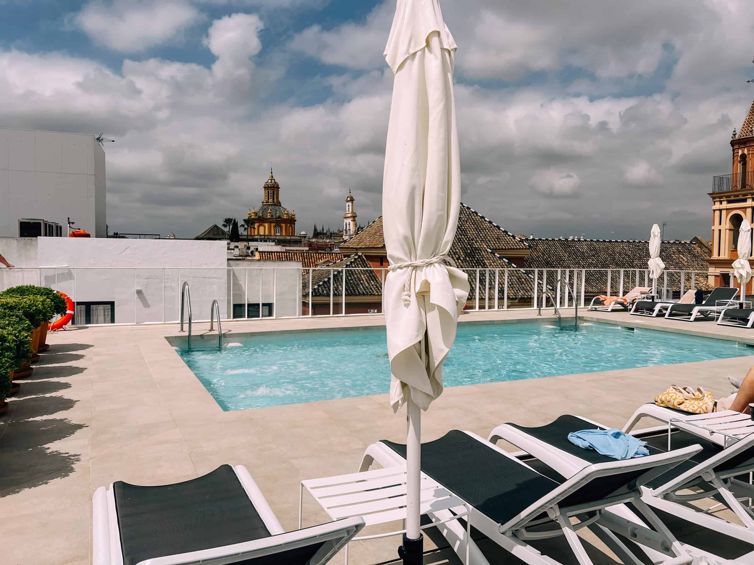 Rooftop pool and sunbeds with city rooftops and church domes beyond.