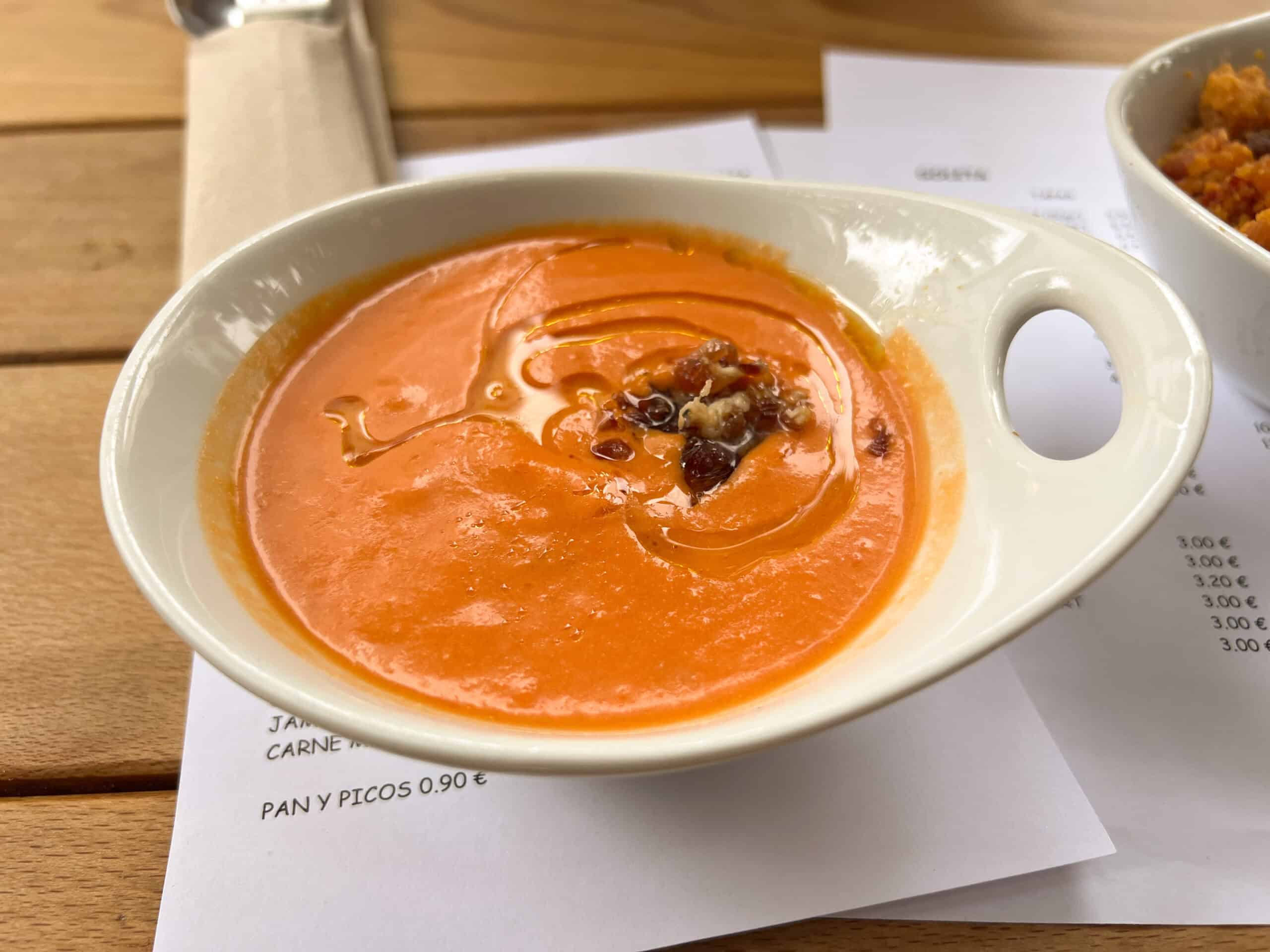 Bowl of Salmorejo served on a wooden table at a tapas bar.